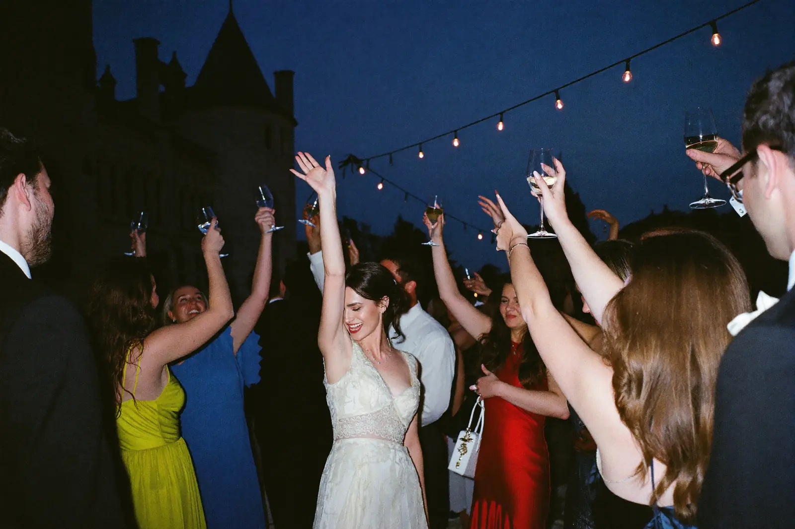 Invités levant leurs verres autour de la mariée, terrasse d’un château à la tombée du soir